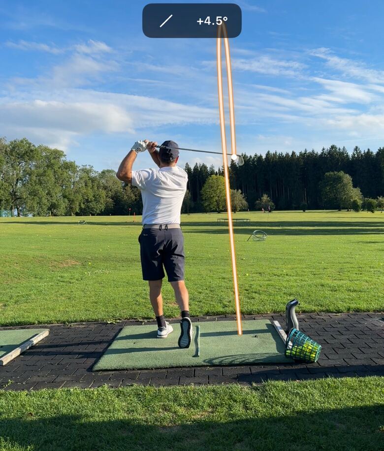 Swing video with the ball tracer: a golfer in the finish on a driving-range mat, the computed flight of the shot drawn as an orange line into the sky